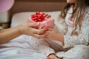 avvicinamento mani di donna e bambino, Tenere regalo scatola con rosso arco. madre dà un' contento presente per sua bello figlia foto