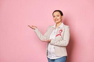 incinta donna, indossare rosa raso nastro - emblema di combattente Seno cancro, mostrando copia spazio su isolato sfondo foto