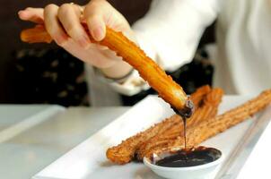 femmina mano godendo immersione churros per buio cioccolato salsa foto