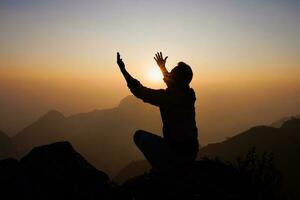 silhouette di un' uomo è preghiere per Dio su il montagna. preghiere mani con fede nel religione e credenza nel Dio su benedizione sfondo. energia di speranza o amore e devozione. foto