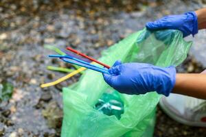 mano di donna raccolta su plastica cannucce in spazzatura borse mentre pulizia piccolo fiume. volontariato, beneficenza, le persone, ecologia concetto. avvicinamento volontario raccolta plastica spazzatura nel foresta. foto