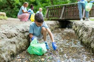 ragazzo ragazzo raccolta manuale raccolta su spazzatura plastica cannucce spazzatura a partire dal il fiume a il parco. mondo ambiente giorno.ambiente concetto. foto