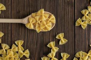 crudo pasta farfalle su cucchiaio su di legno sfondo. foto