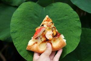 mano Tenere fetta di Pizza su loto le foglie sfondo. italiano cibo foto