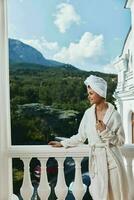 attraente giovane donna nel un' bianca accappatoio su il balcone po su verde natura rilassamento concetto foto