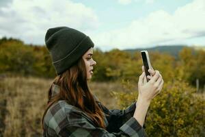 donna nel natura con un' mobile Telefono e un' scacchi camicia cappello su sua testa foto