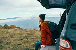 donna turista con un' zaino si siede su il tronco di un' auto nel il montagne nel autunno nel natura foto