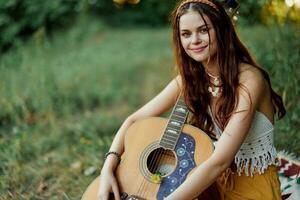 hippie donna sorridente e abbracciare sua chitarra nel natura nel il parco nel il tramonto leggero foto