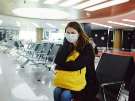 donna nel medico maschera con bagaglio aeroporto in attesa volo ritardo foto