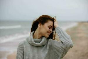 bellissimo donna nel un' maglione volante capelli di il oceano turismo stile di vita foto