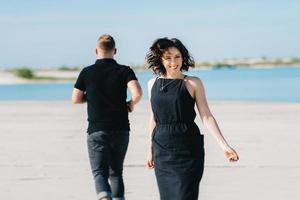giovane coppia un ragazzo con una ragazza in abiti neri stanno camminando sulla sabbia bianca