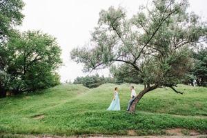 ragazzo felice in una camicia bianca e una ragazza in un vestito turchese stanno camminando nel parco della foresta foto