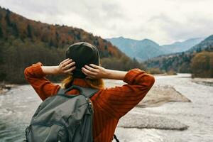 donna viaggiatore su vacanza nel il montagne nel natura vicino il fiume hold mani dietro a sua testa foto