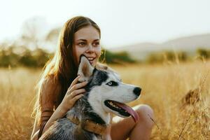 donna e sua rauco cane felicemente passeggiare attraverso il erba nel il parco Sorridi con denti autunno tramonto camminare con animale domestico, viaggio con un' cane amico foto