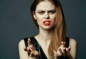 un' donna nel un' nero vestito con rosso labbra gesti con sua mani perplesso Guarda grigio sfondo foto