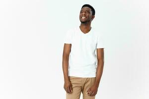 contento africano uomo nel bianca maglietta e beige pantaloni su leggero sfondo ritagliata Visualizza foto