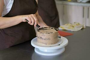 donna Pasticcino capocuoco Linee cioccolato crema su cioccolato torta, avvicinamento. torta fabbricazione processi, selettivo messa a fuoco foto