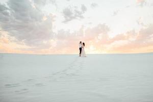 giovane coppia un ragazzo in calzoni neri e una ragazza in un vestito rosa stanno camminando lungo la sabbia bianca