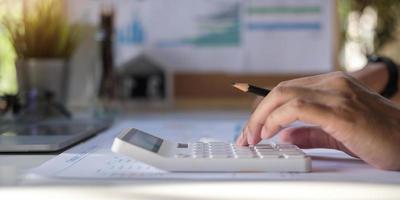 primo piano di un uomo d'affari che calcola la fattura utilizzando la calcolatrice sul posto di lavoro foto