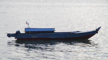 piccolo lungo di legno il motore barca per pesca e trasporto legato su o ancorato a il superficiale mare. foto