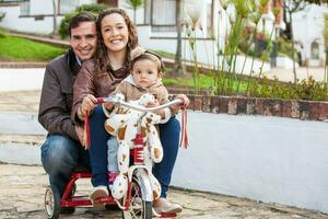 uno anno vecchio bambino all'aperto equitazione sua triciclo con sua genitori. foto