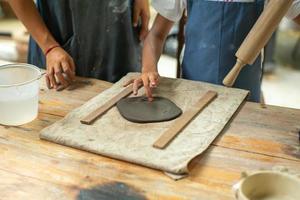 Stretta di mano di una ragazza utilizzando un mattarello su argilla durante la lezione di laboratorio di stampaggio foto