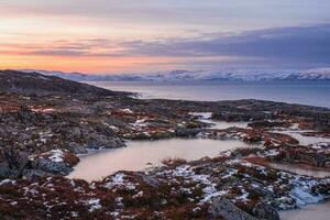 meraviglioso montagna paesaggio con un' capo su il riva di il barents mare. sorprendente Alba paesaggio con polare bianca nevoso gamma di montagne. foto