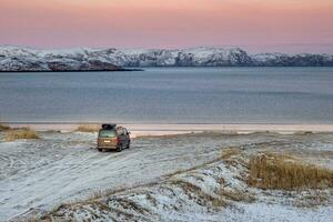 il auto è parcheggiata su il riva di il artico oceano. viaggio concetto di in viaggio di macchina. sorprendente Visualizza di il settentrionale baia nel il villaggio di teriberka foto