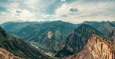 eccezionale panoramico Visualizza a partire dal passaggio per montagna valle nel luce del sole e grande montagna sagome su orizzonte. colorato soleggiato verde paesaggio con sagome di grande roccioso montagne e epico in profondità gola foto