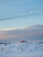 solitario bungalow ander pieno Luna su un' nevoso montagna pendenza sotto un' luminosa alba cielo. verticale Visualizza. foto