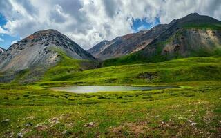 panoramico alpino paesaggio con bellissimo superficiale montagna lago con flussi nel montanaro verde valle a partire dal più grande montagne sotto nuvoloso cielo. piovoso montagna scenario con specchio glaciale lago. foto