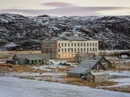 autentico villaggio di teriberka nel il nord di Russia. il edificio di un vecchio abbandonato scuola contro il fondale di artico colline nel inverno foto