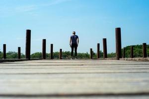 indietro ritratto di uomo bello in panno casual si trova sul ponte di legno con lo sfondo del cielo blu foto