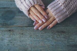 donne è mani con un' bellissimo manicure, nel un' a maglia maglione su un' di legno sfondo in. autunno tendenza, polacco il beige e Quaglia uovo modello su il Chiodi con gel polacco, Gommalacca. copia spazio. foto