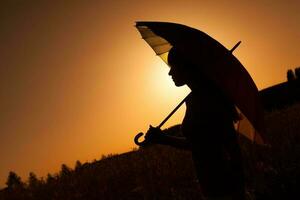 silhouette di un' donna con ombrello al di sopra di il tramonto foto