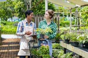 giovane caucasico cliente è chiede il asilo proprietario di il esotico pianta con shopping carrello pieno di estate pianta per fine settimana giardinaggio e all'aperto concetto foto