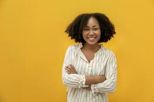 ritratto studio tiro di africano americano donna sorridente nel casuale stoffa con grande Sorridi e attraversato mano isolato su giallo sfondo guardare a telecamera per casalinga e alunno fiducia concetto foto