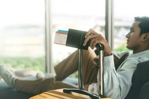 viaggiatore asiatico uomo braccio Tenere bagaglio maniglia passaporto e prenotazione aereo biglietto foto
