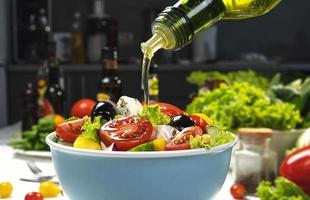 versando olio d'oliva su insalata di verdure fresche foto