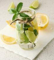 limonata nel un' trasparente bicchiere con Limone, lime, rosmarino rametti e menta le foglie su un' bianca sfondo foto