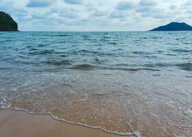 Visualizza di il spiaggia e onde con il fondale di il isola e il nuvole. foto