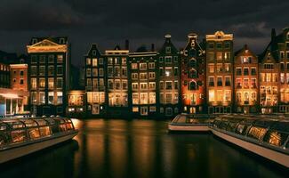 notte scena con sorprendente architettura e Barche nel canale a amsterdam città, Olanda foto