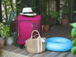 viaggio Accessori, rosa bagaglio, intrecciata Borsa, zaino, cuffia, nuoto squillare e cannuccia cappello su balcone con pianta della casa. foto