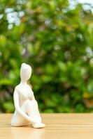 ceramica yoga figurina di donna fare yoga posa su di legno pavimento e verde foglia sfondo foto