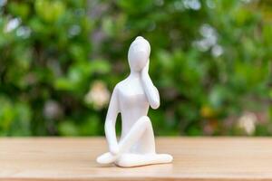 ceramica yoga figurina di donna fare yoga posa su di legno pavimento e verde foglia sfondo foto