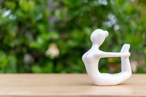 ceramica yoga figurina di donna fare yoga posa su di legno pavimento e verde foglia sfondo foto