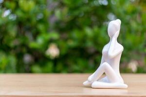 ceramica yoga figurina di donna fare yoga posa su di legno pavimento e verde foglia sfondo foto