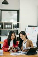 Due asiatico donna d'affari discutere investimento progetto Lavorando e pianificazione strategia con tavoletta il computer portatile computer nel ufficio. foto