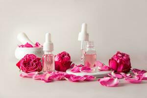 naturale essenziale olio per casa pelle cura. rosa fiori. cosmetico bicchiere bottiglie con il Prodotto, un' mortaio con un' pestello e rosa petali. foto