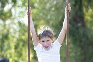 il ragazzo cavalcate su un' swing nel il estate contro il fondale di verde. foto